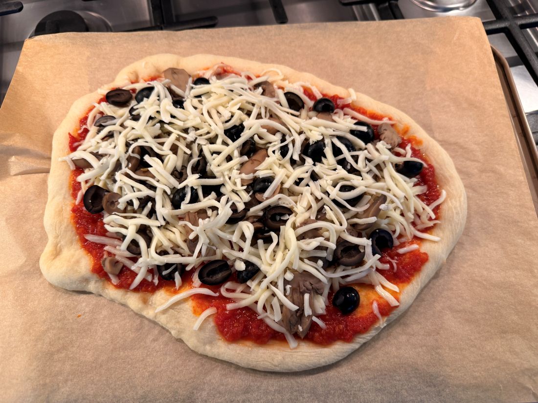 The pizza assembled with sauce, cheese, and vegetables, ready to slide back into the oven
