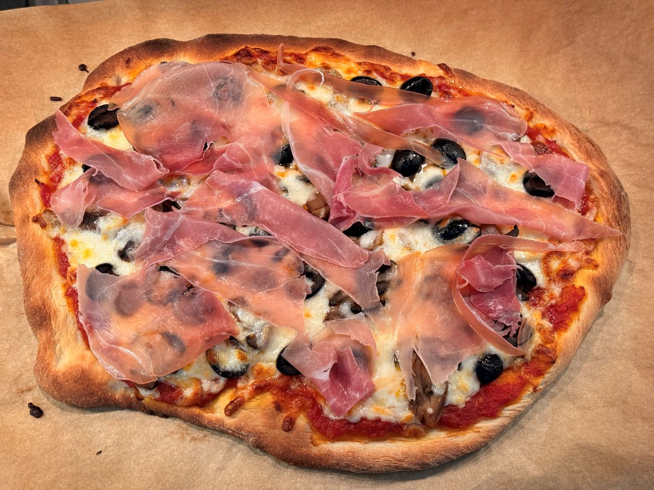 The finished, golden-brown pizza topped with fresh prosciutto and sliced